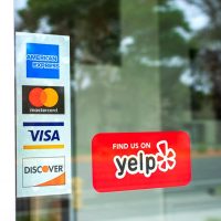 MasterCard, VISA, American Express, Discover payment options advertised on a restaurant door. A red sticker decal promotes Yelp crowd-sourced reviews service - San Francisco, California, USA - 2020
